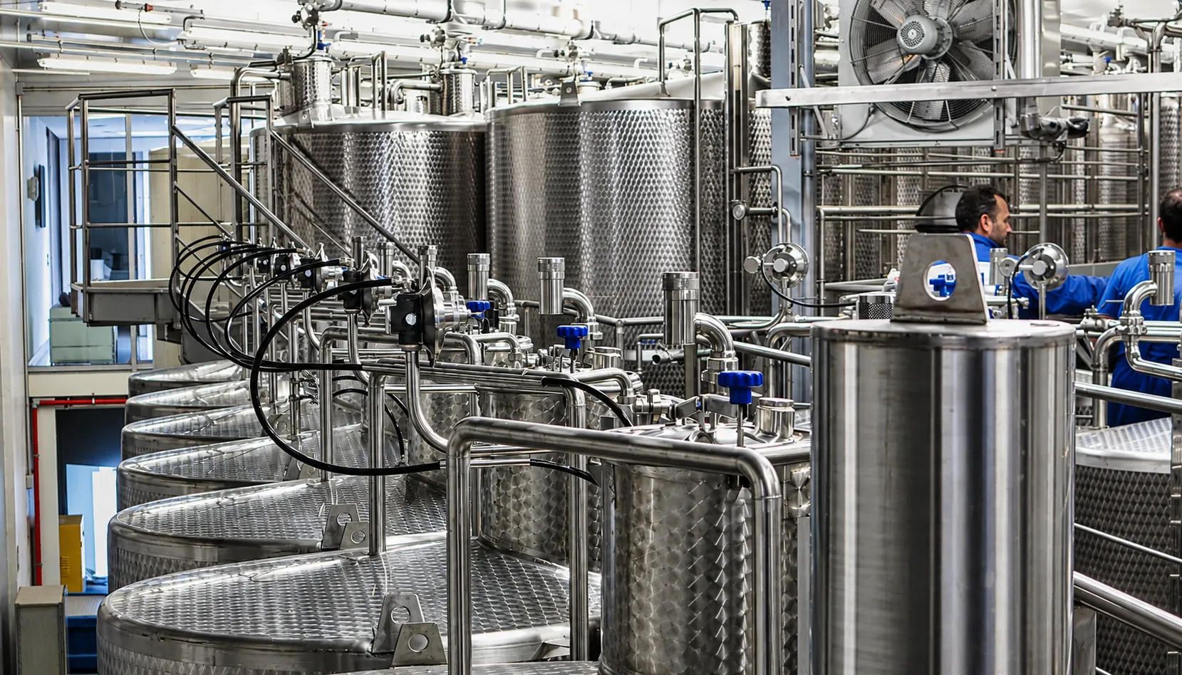 Linea di lavorazione alimentare con serbatoi inox e operatori in sala produzione